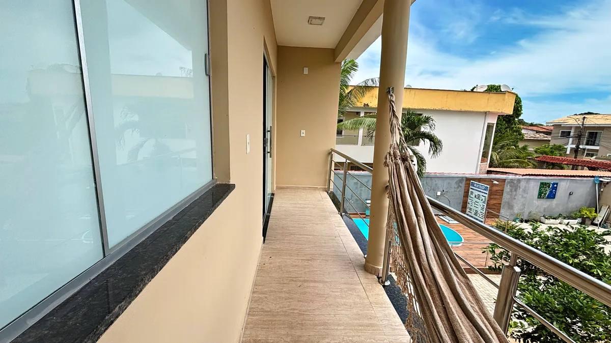 Varanda lateral com piso de porcelanato, guarda-corpo de vidro e vista da piscina e ceu azul