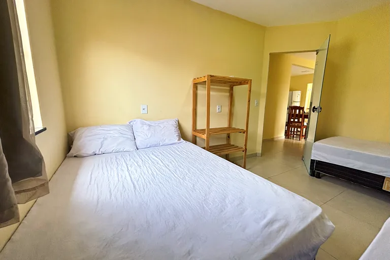 Quarto de casal cama com lencol branco e estante de madeira