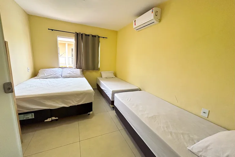 Quarto com cama de casal e camas de solteiro ar condicionado e janela