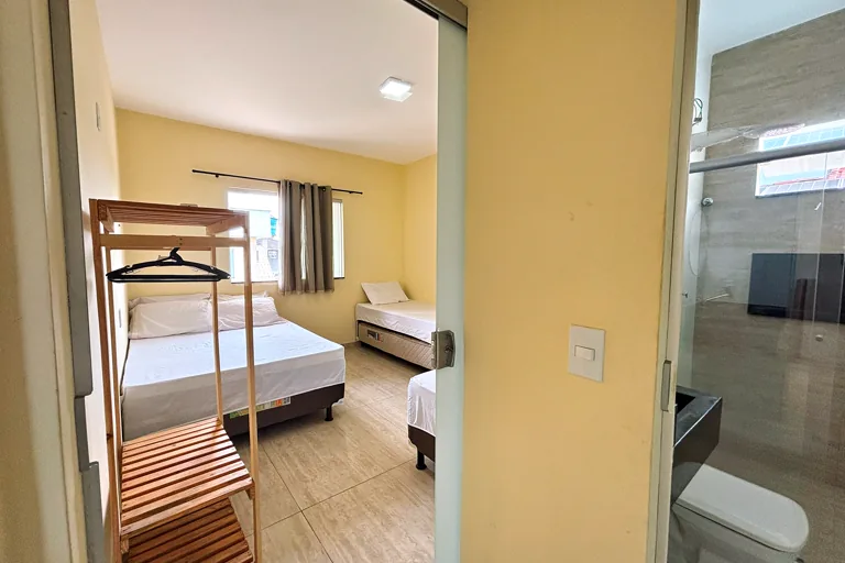 Visao da entrada do quarto com camas e banheiro de vidro ao lado