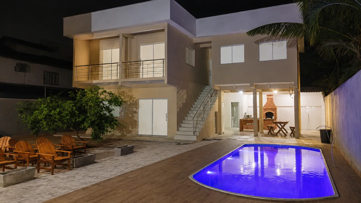 Area externa da Casa Hortela a noite, com sobrado iluminado, area coberta e a piscina compartilhada do residencial