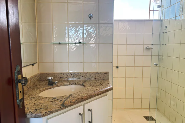 Banheiro com bancada de granito espelho e box de vidro com chuveiro