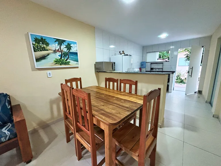 Sala de jantar da Casa Pitanga com mesa de madeira macica e quadro tropical