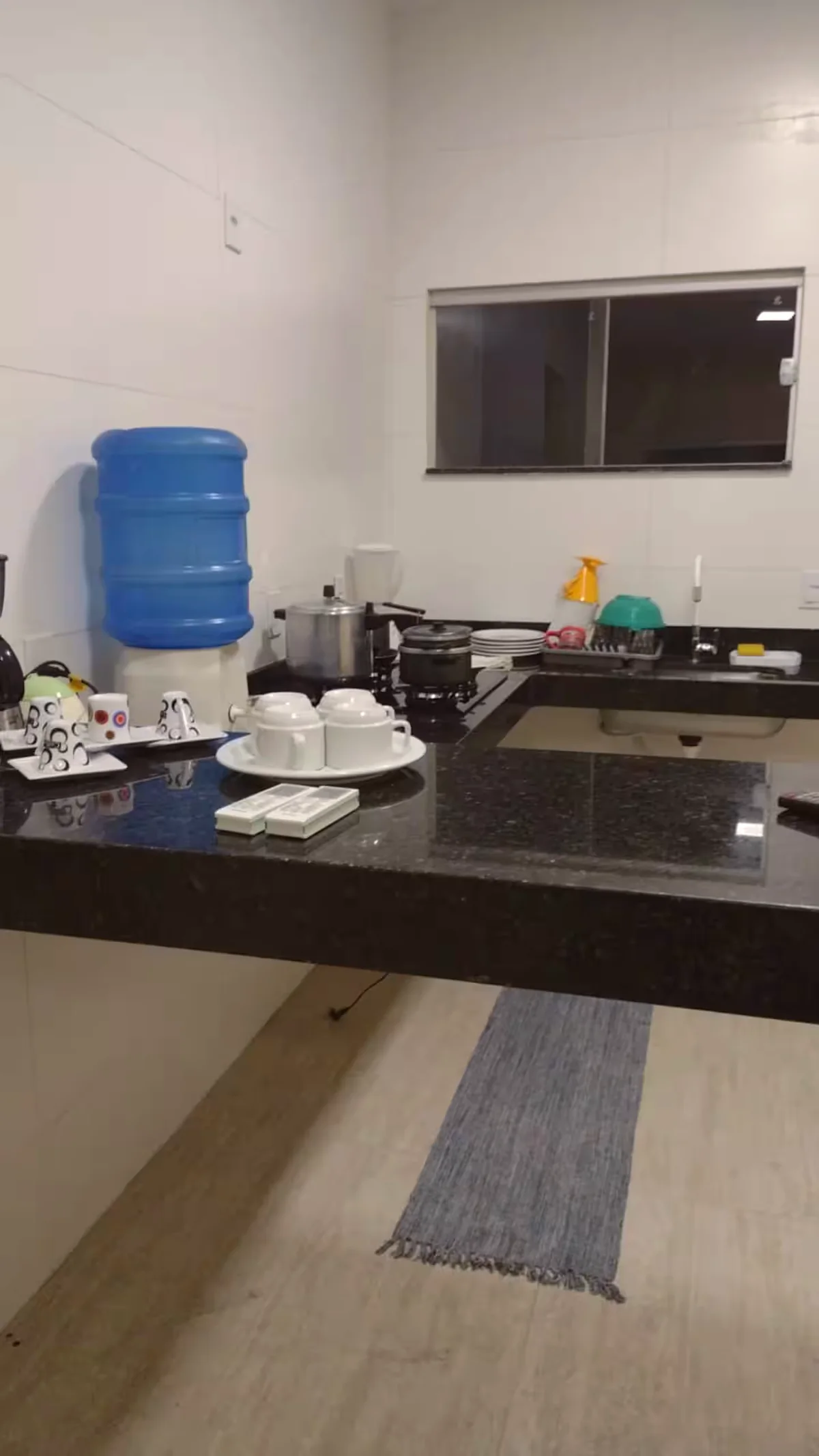 Cozinha com bancada preta, pia, fogao e utensilios sobre a bancada.