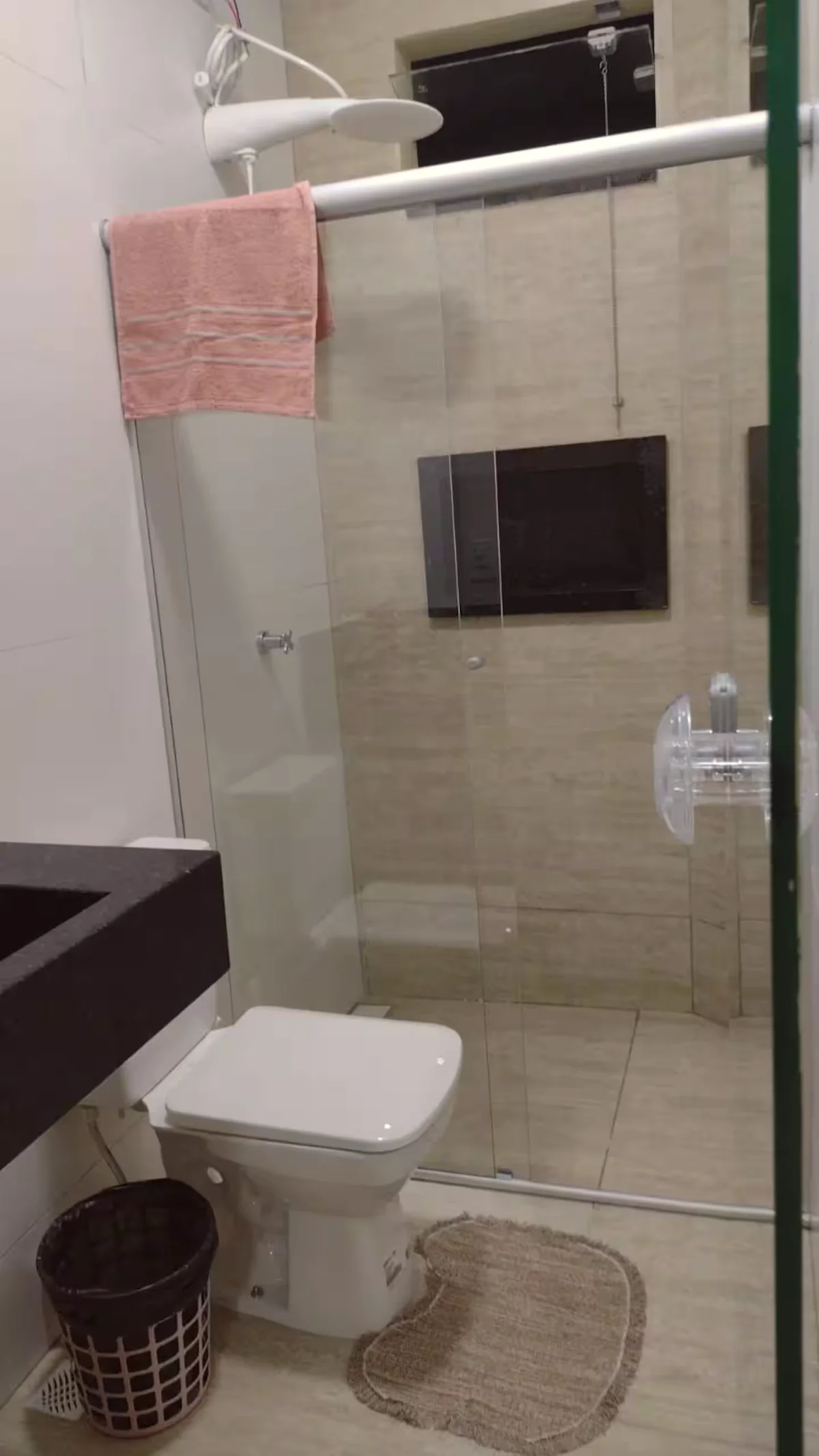 Banheiro com box de vidro, vaso sanitario e bancada preta.