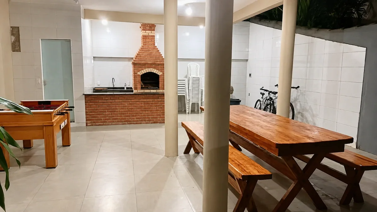 Area coberta com mesa de madeira, churrasqueira de tijolos e mesa de jogos.