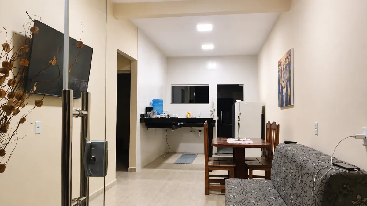 Sala integrada da Casa Capim Santo com sofa, mesa de jantar, TV e cozinha ao fundo.