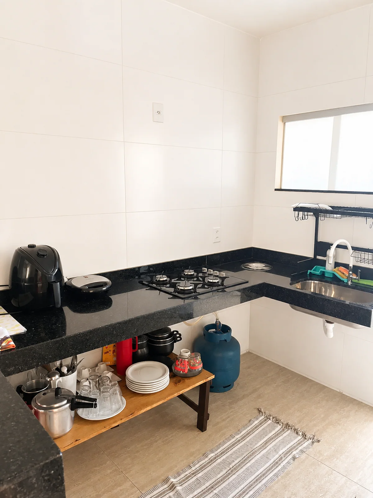 Cozinha com bancada preta, cooktop, pia, pratos e utensilios.