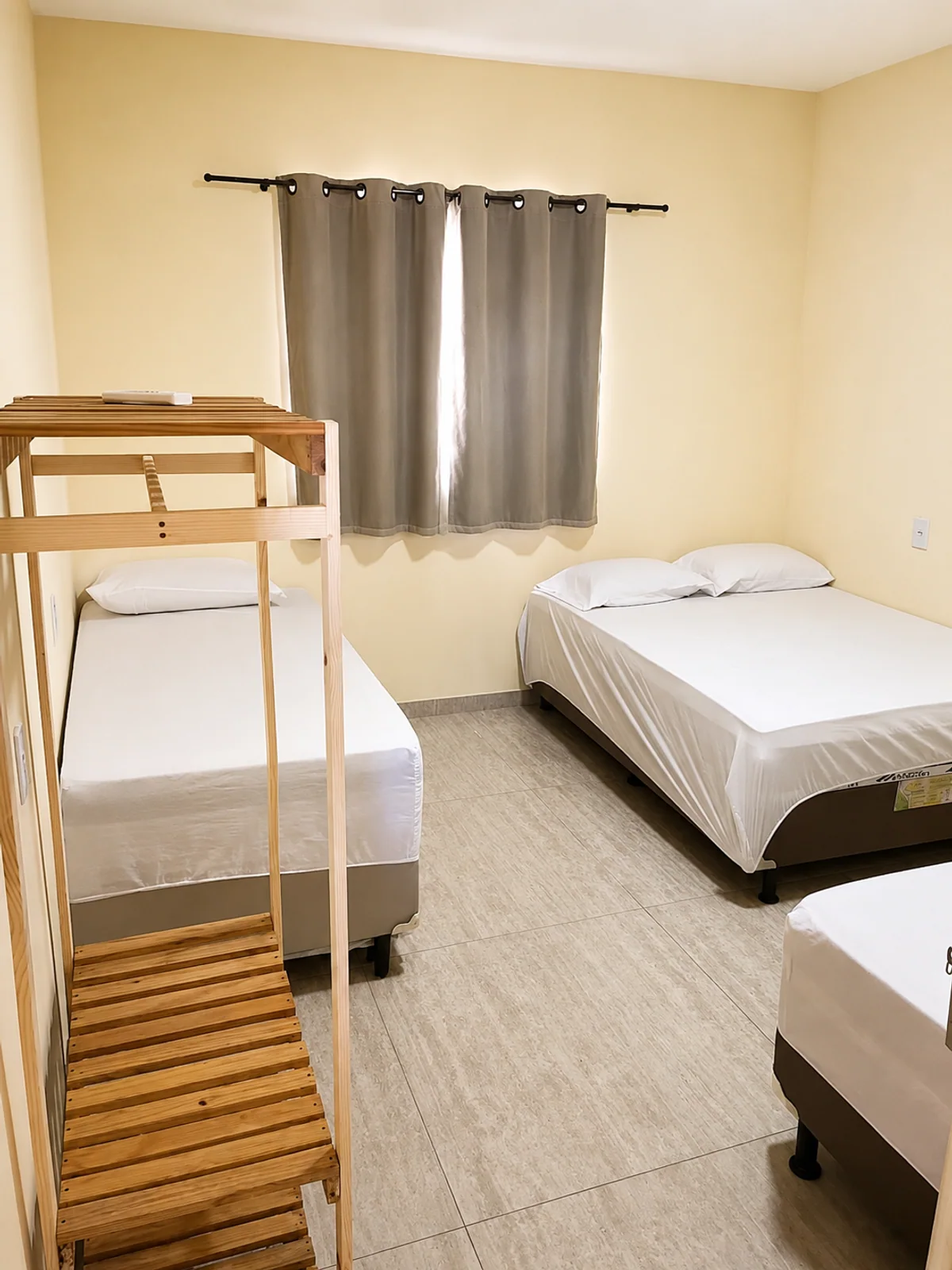 Quarto com beliche de madeira, cama de casal e cama de solteiro.