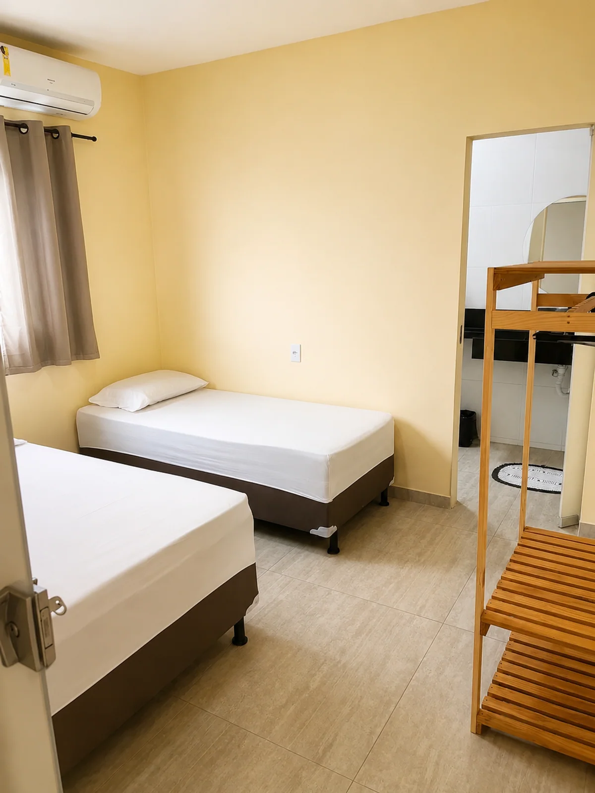 Quarto com duas camas de solteiro, beliche de madeira e ar-condicionado.