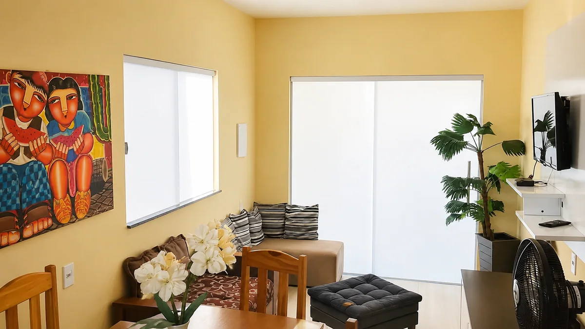 Sala da Casa Eva Doce com sofa, mesa de jantar, TV e planta decorativa.