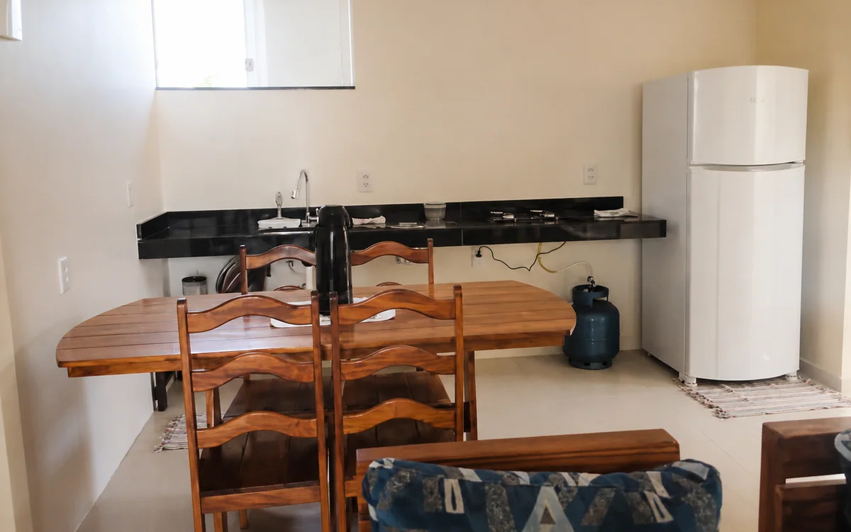 Sala de jantar integrada a cozinha com geladeira, bancada e mesa de madeira.