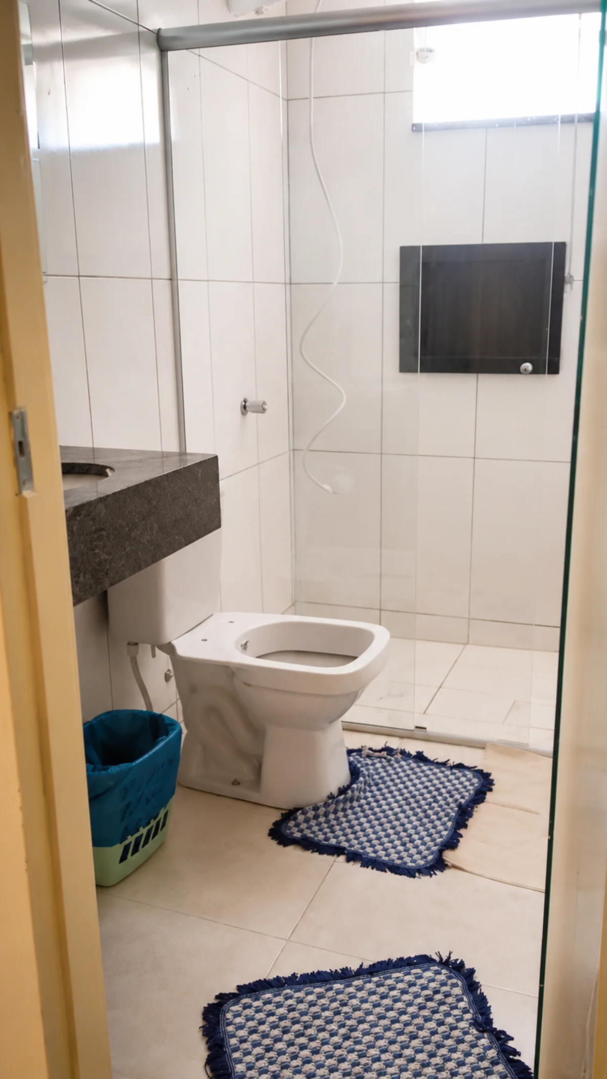 Banheiro com box de vidro, vaso sanitario e pia com bancada escura.