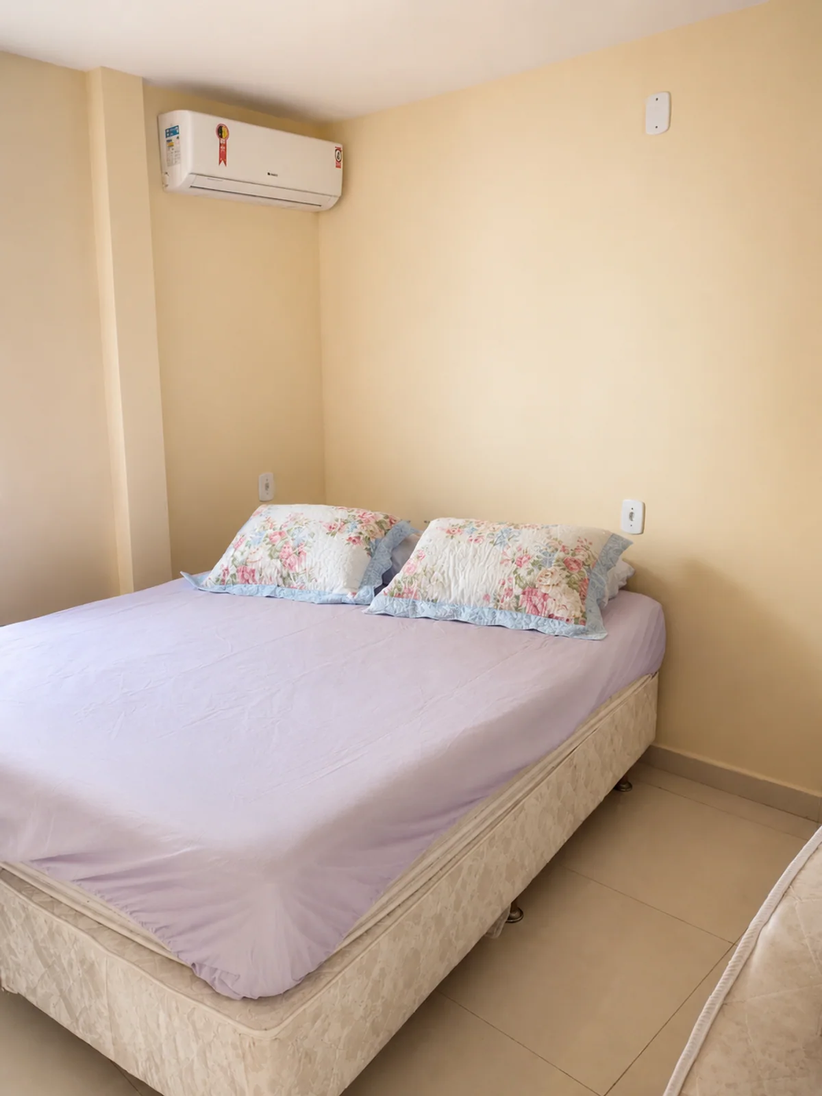 Quarto com cama de casal, ar-condicionado e roupa de cama clara.
