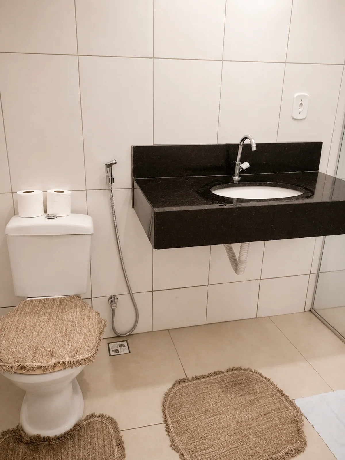 Banheiro com vaso sanitario, pia com bancada preta e box de vidro.