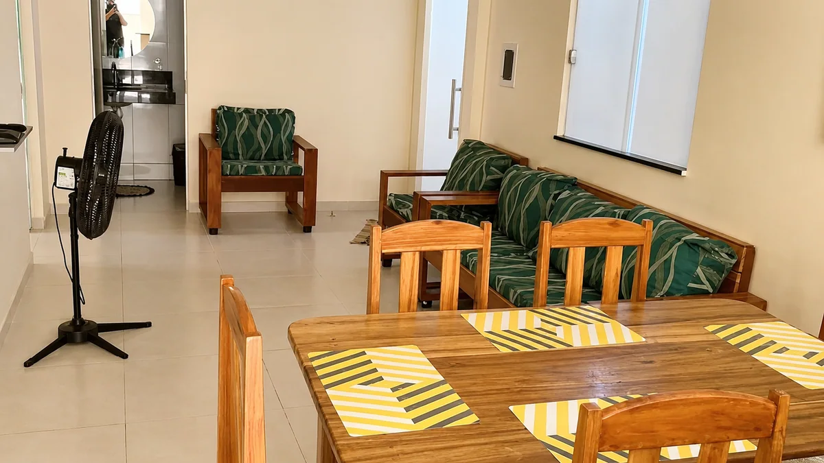 Sala e jantar da Casa Pitanga com mesa de madeira, sofa, poltrona e ventilador.